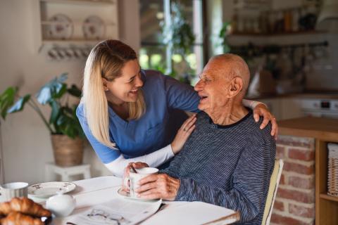 Female caregiver and older man at breakfast table facing each other smiling