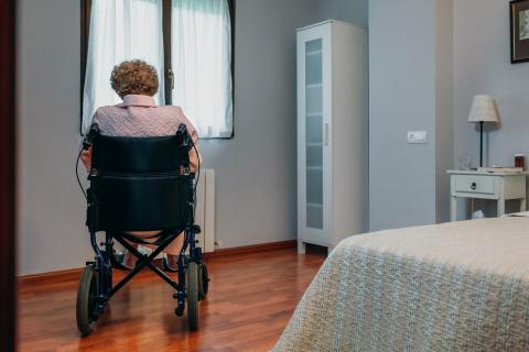 Elderly woman sitting in a wheelchair facing the window in a bedroom