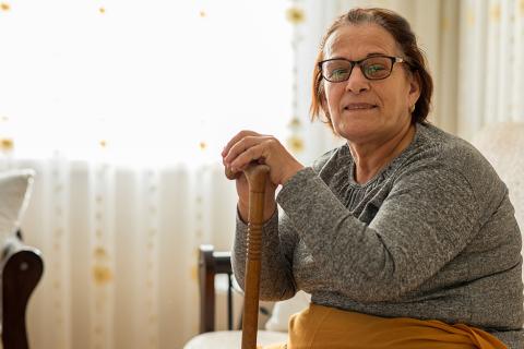 older woman wearing glasses sitting while holding a cane
