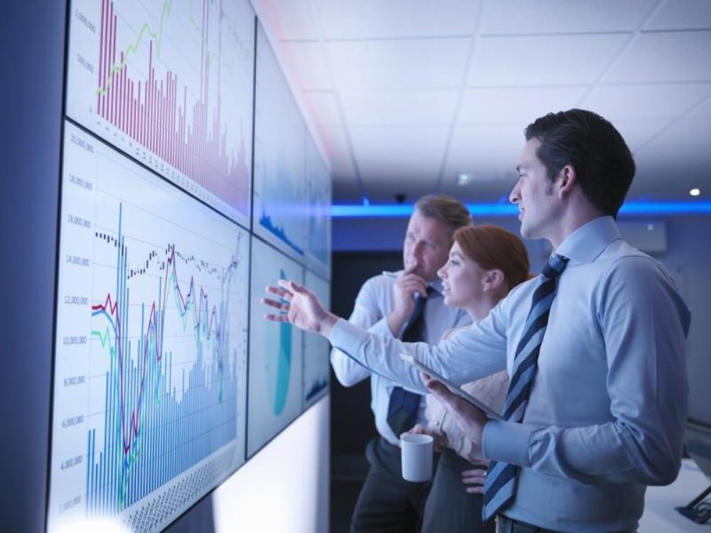 Three businesspeople standing in front of large data screens in conference room