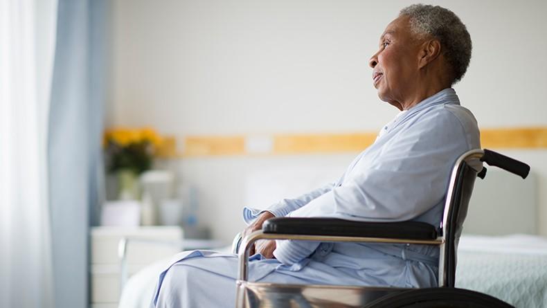 African American senior in wheelchair in hospital room smiling while looking out the window