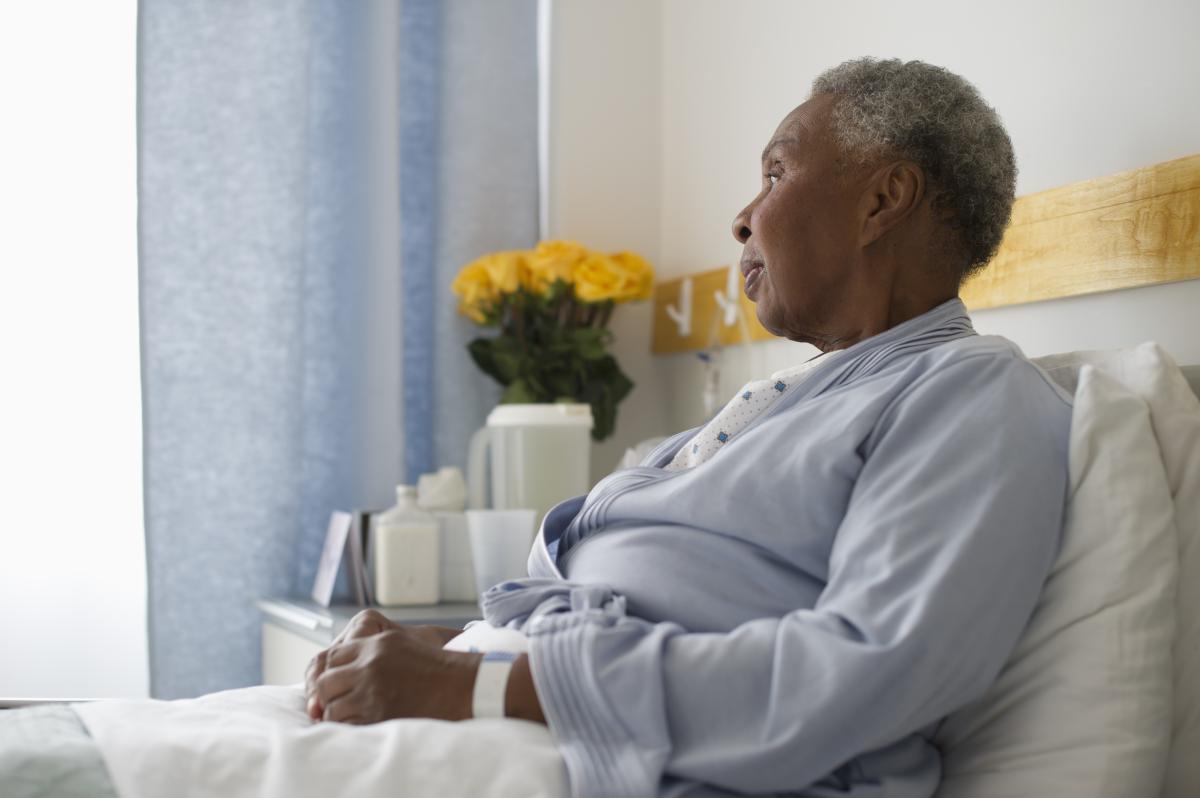 african american woman sitting in nursing home bed yellow roses on bedside table